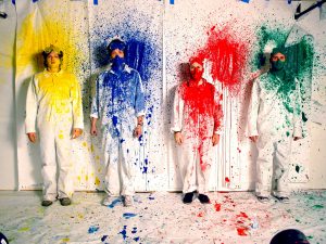 Snapshot of Ok Go band members splattered with multi-colored paint from music video