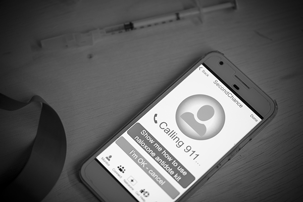 The smartphone interface shows the Second Chance app dialing 9-1-1 for emergency intervention after detecting signs of an overdose