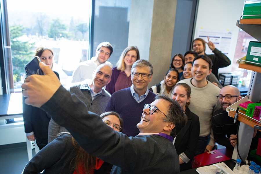 A group of faculty and students gather and pose for a selfie with Bill Gates in a lab.