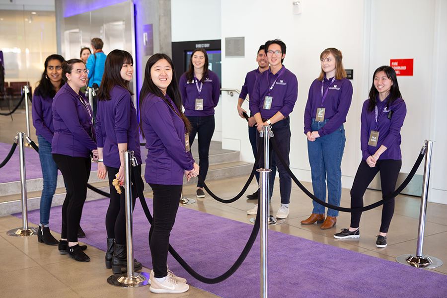 Two rows of smiling college students dressed in purple Allen School-branded shirts flanking the purple carpet, waiting to welcome guests to the dedication event.