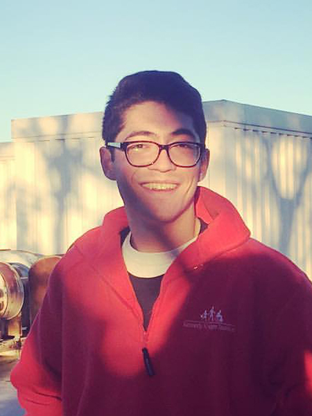 Benjamin Lee in glasses and red jacket smiling in front of industrial building