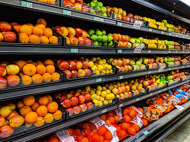 Grocery store produce shelves filled with different varieties of fruit, including apples, oranges, lemons and pears.
