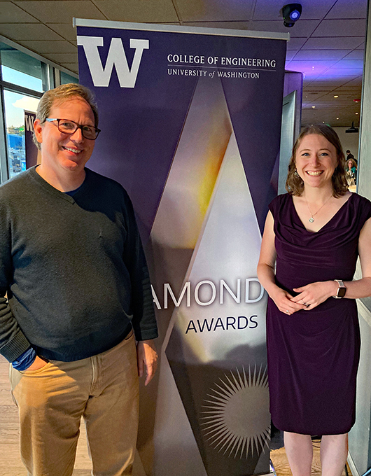Stefan Savage (left) and Justine Sherry (right) stand either side of a large sign with UW block "W" logo, College of Engineering logo and partially visible text "Diamond Awards" superimposed on diamond graphic.
