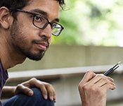 Vikram Iyer wearing glasses holding tweezers in his right hand, crouched
