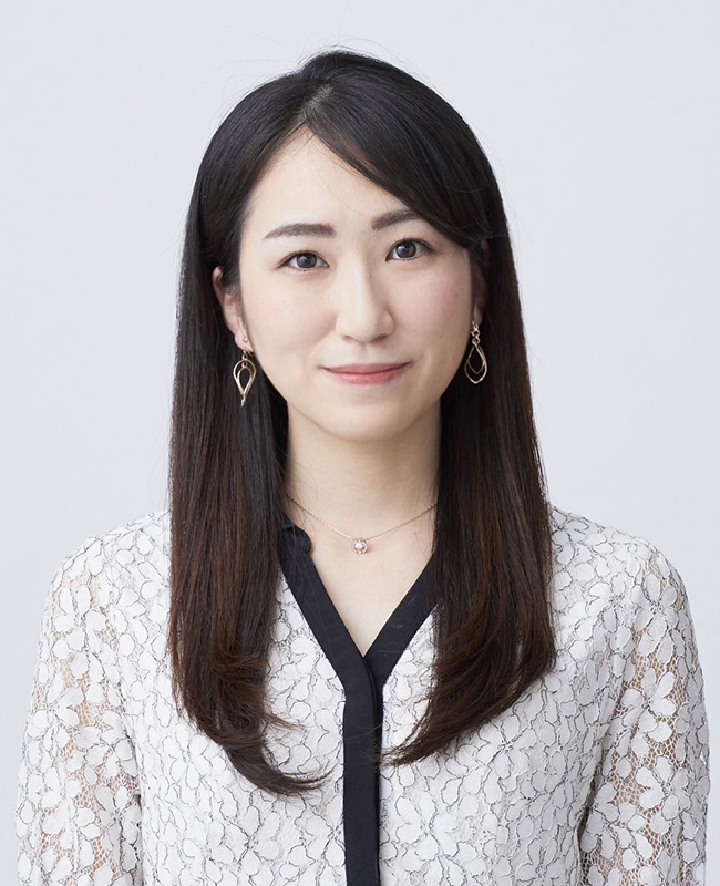 Portrait of Akari Asai wearing grey floral lace top with black trim and dangling earrings against a grey background