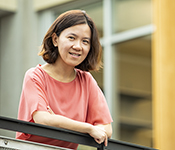 Portrait of Rachel Lin leaning against a metal railing in building atrium with concrete, wood and glass in the background