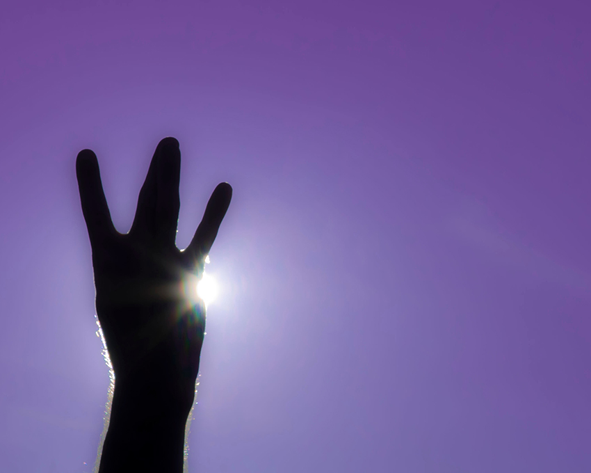 Hand silhouetted against the sun, giving the "dubs up" symbol, with ring and middle finger crossed in between pinky and index finger to resemble the letter "W," against a purple background