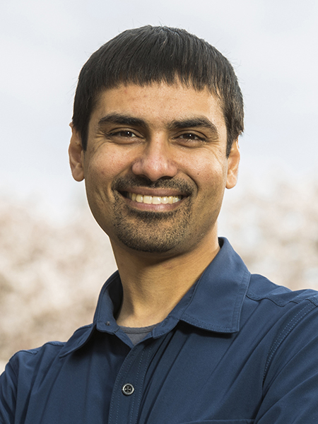 Shwetak Patel wearing dark blue button-down shirt with blurred cherry blossoms and pale blue sky in the background