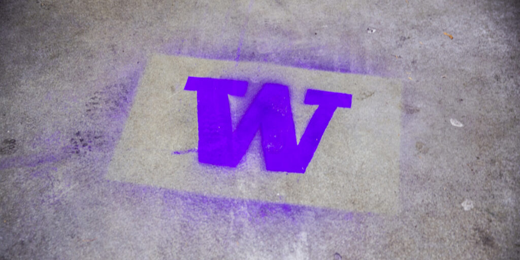 Graffiti-style UW block "W" logo stenciled and spray-painted in bright purple on concrete surface.