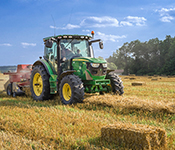 A green tractor harvesting and baling hay in a field under a blue sky