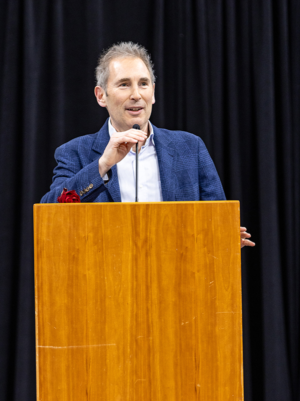Andy Jassy smiles as he speaks into a microphone attached to wooden podium