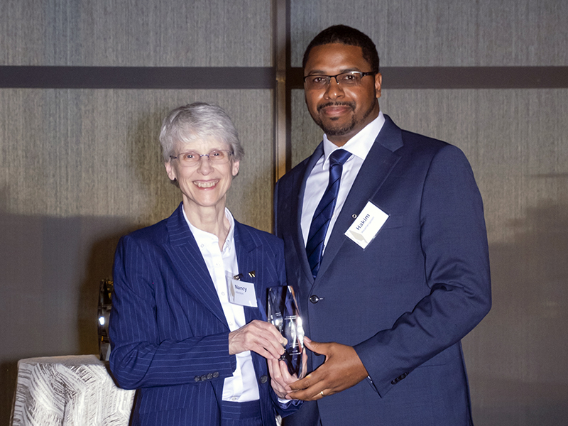 A woman and a man pose smiling for the camera jointly holding a glass award plaque.