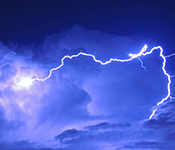 A large bolt of lightning illuminates clouds in a bluish-purple sky