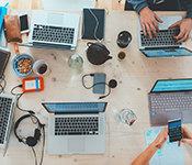 An overhead view of people sitting around laptops and phones working on a project.