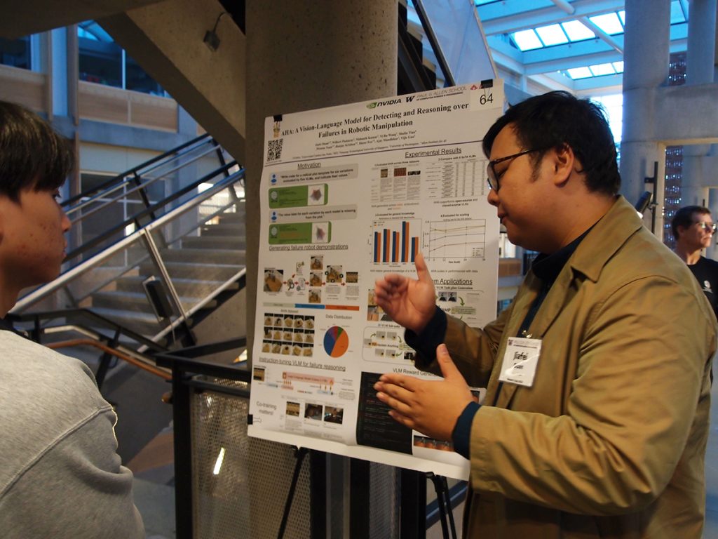 Jiafei Duan gestures as he explains the contents of an adjacent research poster to another person