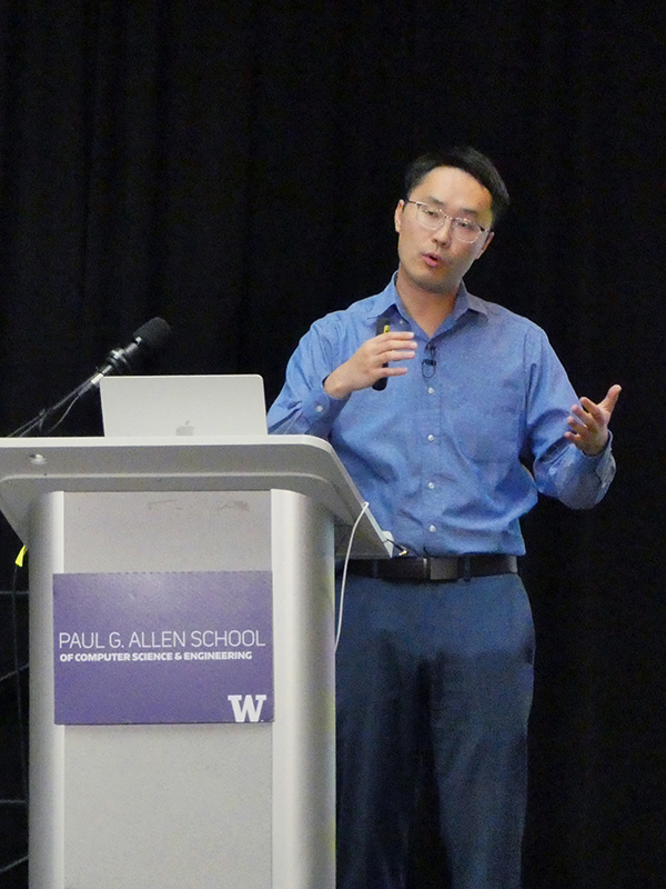 Sheng Wang gestures as he speaks at a podium displaying the Allen School logo