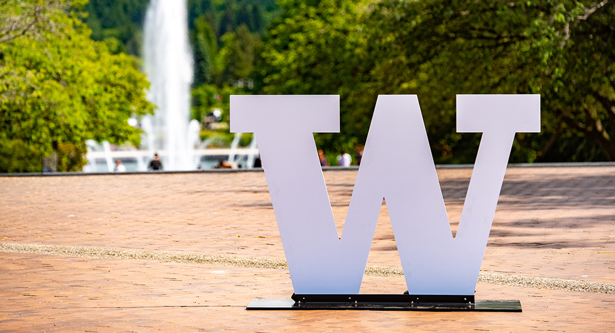 The University of Washington "W" stands in the foreground with the Drumheller Fountain spraying in the background.