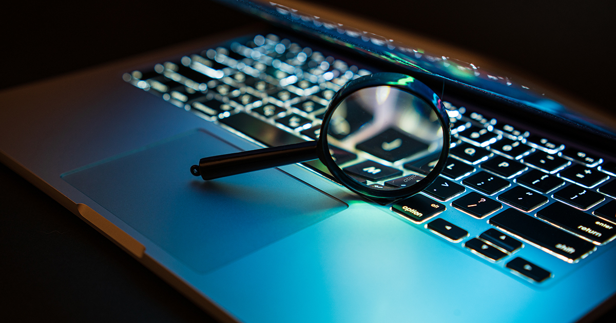 Magnifying glass resting on the keys of a laptop computer