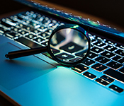 Magnifying glass resting on the keys of a laptop computer